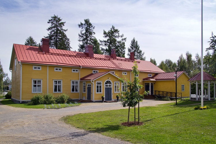 Gårdsplan med gul träbyggnad med rött plåttak.