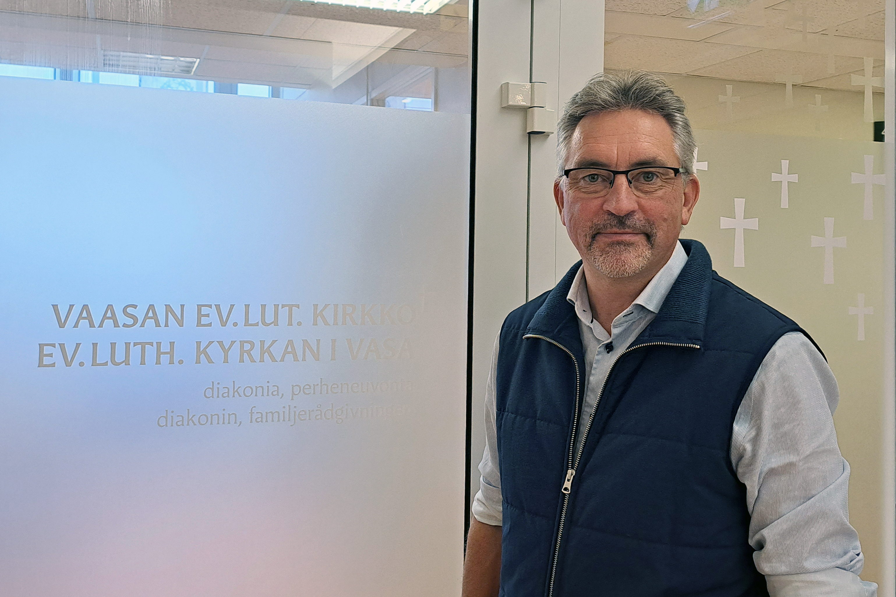 Man står framför en dörr med frostat glas. Text på dörren: Vaasan ev.-lut. kirkko, Ev.-luth. kyrkan i Vasa.