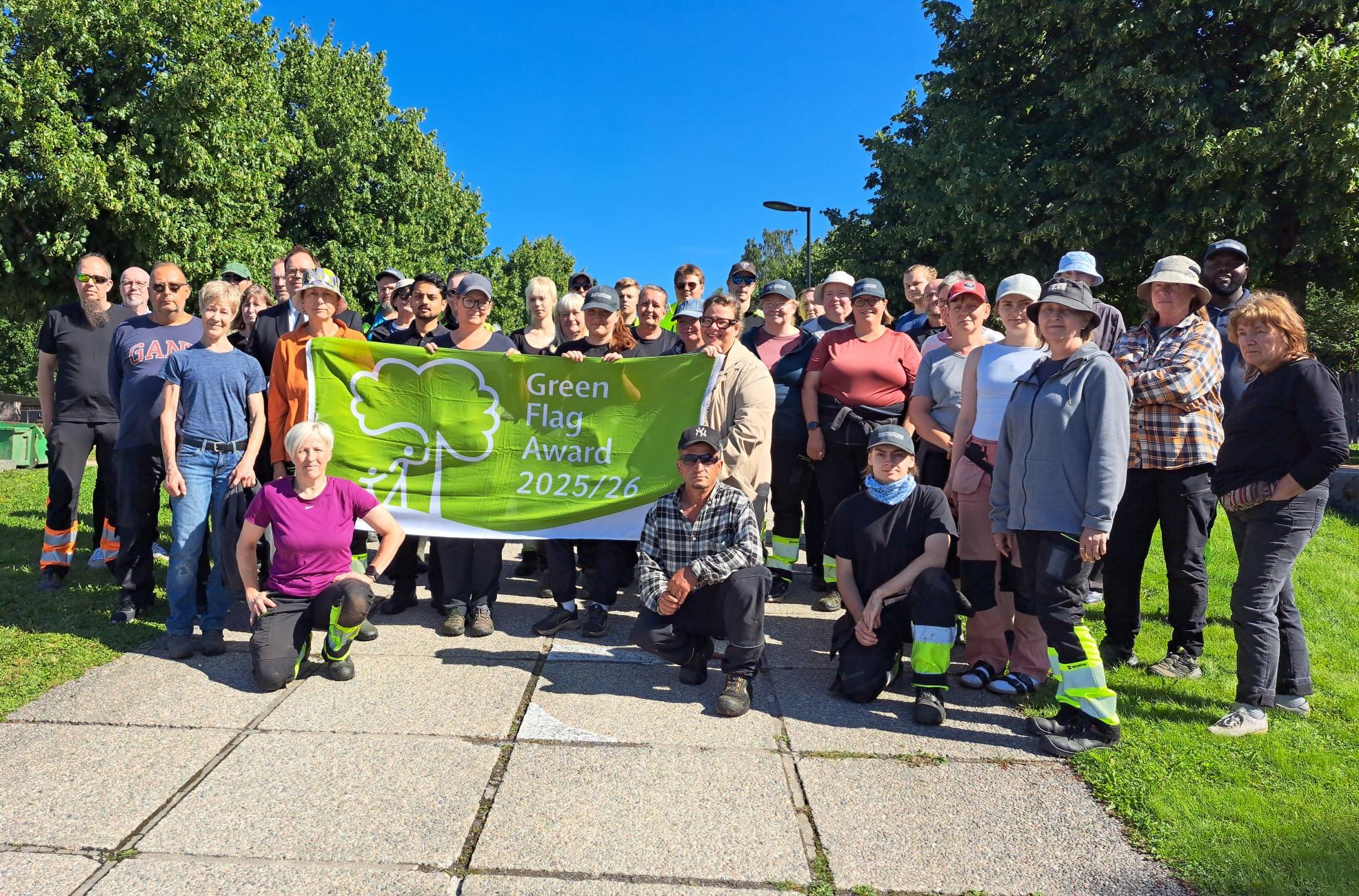 Grupp med människor håller i en grön flagga med texten Green Flag Award 2025/26. Juryn onstaterade att Gaml...