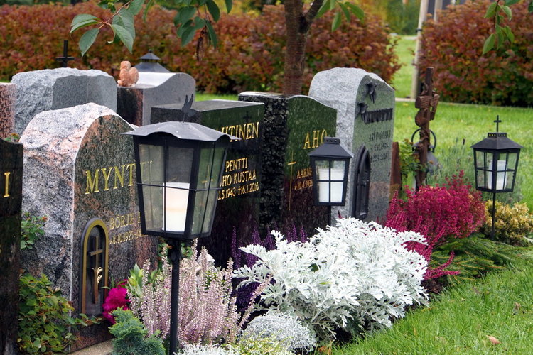 Några gravstenar med blommor och lyktor framför.