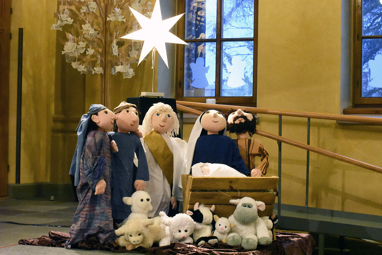 En julkrubba med tygdockor föreställande Jesusbarnet, Maria, Josef, ängel, herdar och får. 