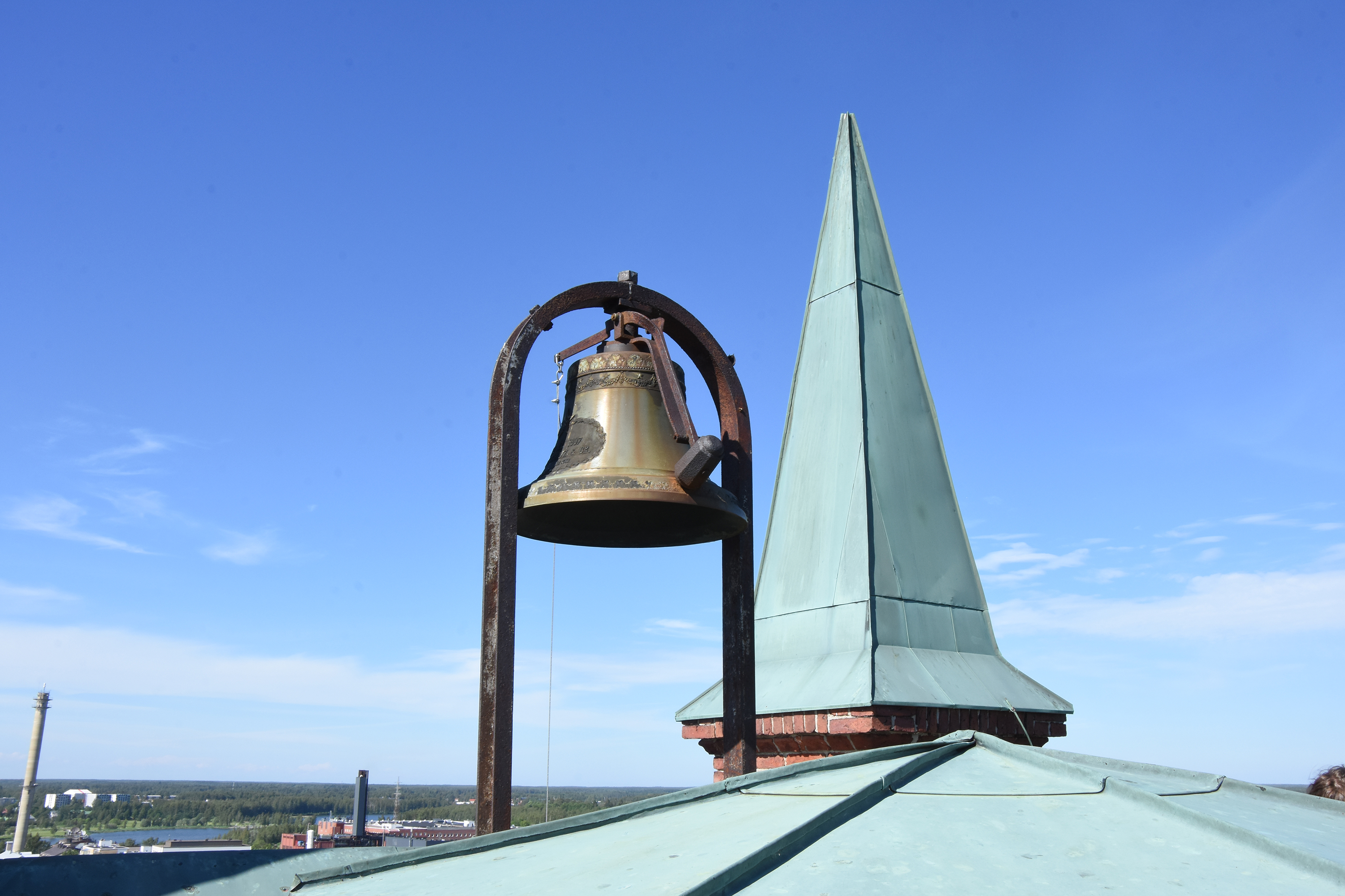 Närbild av kyrkklocka, i bakgrunden syns en kyrkspira.