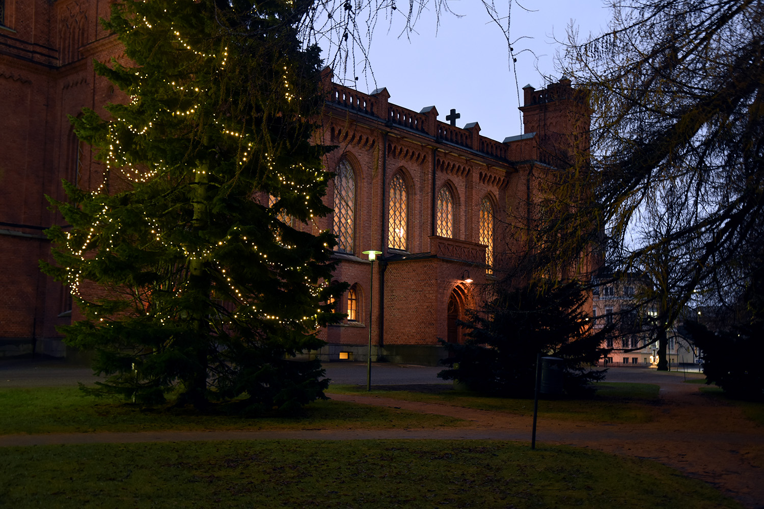 Julgran med belysning utanför en upplyst röd tegelkyrka.